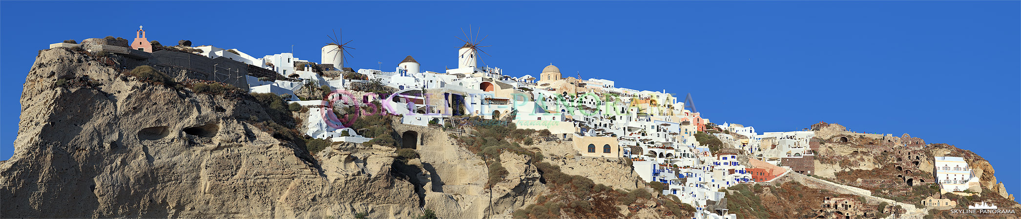 Santorini - Der dicht bebaute Kraterrandfelsen von Oia am westlichen Ende des Kykladendorfes mit den bekannten Windmühlen und dem Lontza-Kastell. 