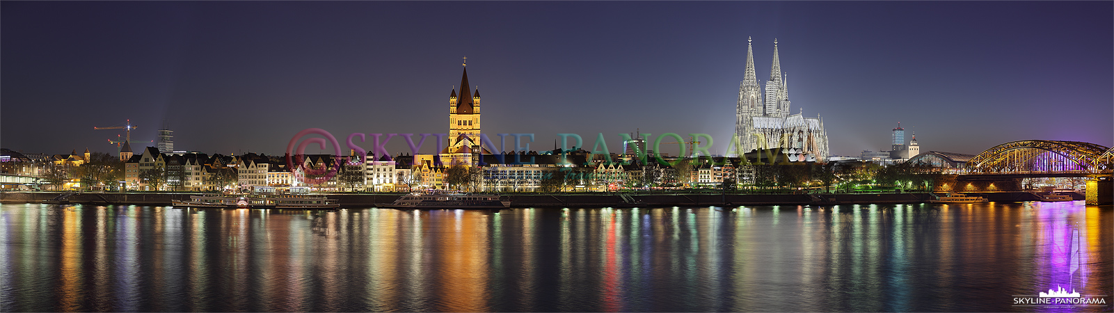 Panorama der abendlichen Kölner Skyline mit dem beleuchteten Kölner Dom und der Kirche Sankt Martin. 