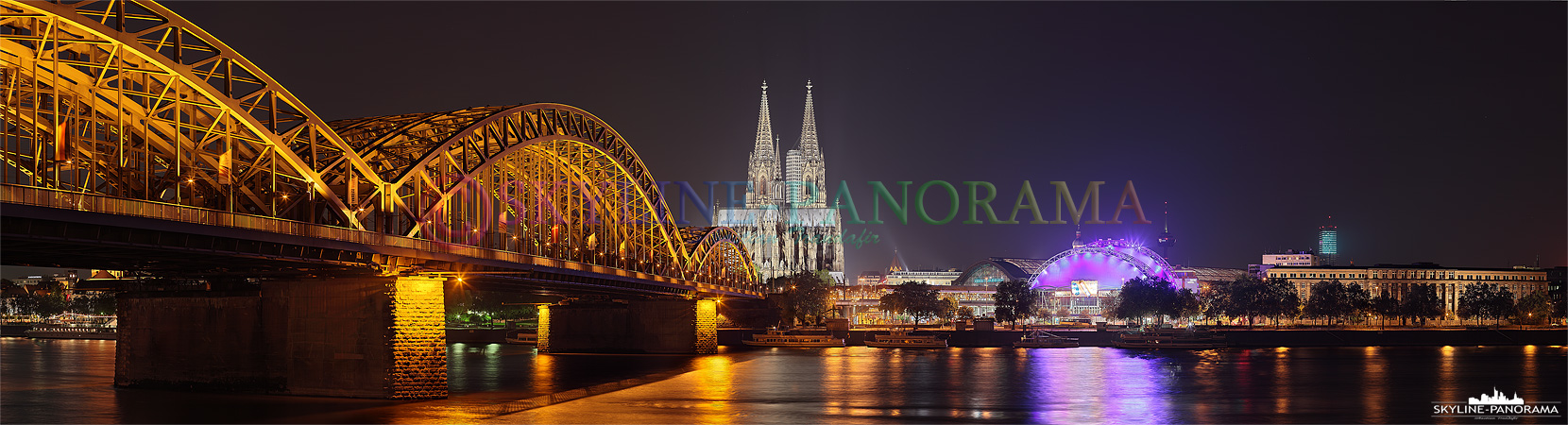 Die Kölner Skyline mit der Hohenzollernbrücke, dem Kölner Dom und dem Musical Dome bei Nacht vom Rheinufer aus gesehen. 