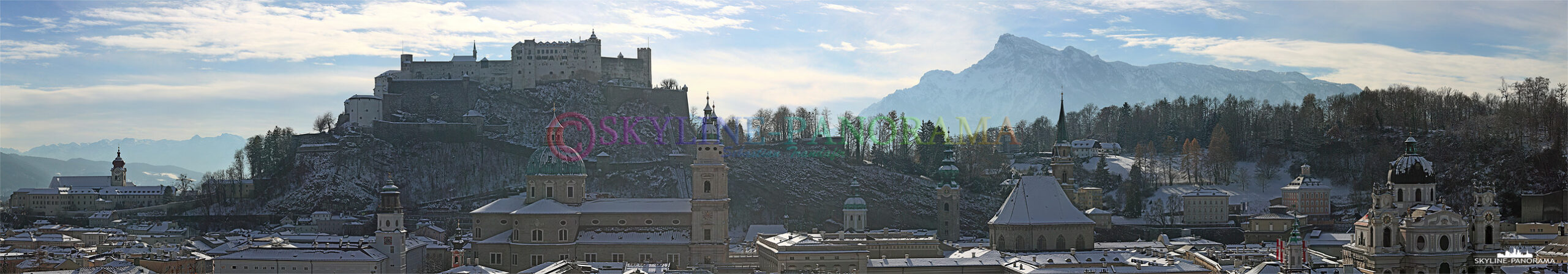 Die verschneiten Dächer der Altstadt von Salzburg mit der Festung Hohensalzburg und dem dahinter liegenden Untersberg.