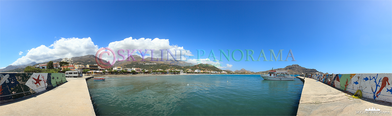 Das Panorama zeigt den Blick aus dem Fischerhafen von Plakias mit dem langen Sandstrand und den Berghängen, die unmittelbar hinter dem Ort aufsteigen.