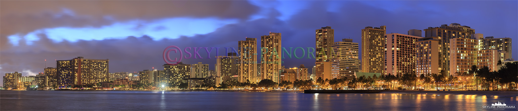 Die Skyline von Honolulu mit zahlreichen Hotels und Hochhäusern im Stadtteil Waikiki - zu sehen ist der Traumstrand mit seiner Promenade als Panorama nach Sonnenuntergang. 