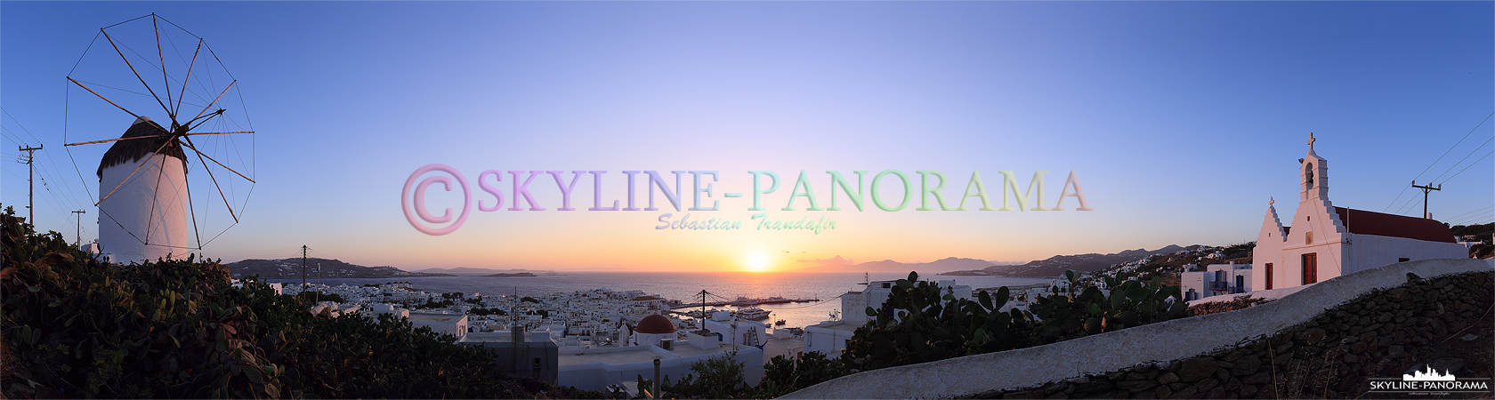 Sonnenuntergang vom Aussichtspunkt an der Windmühle Ano Myli mit einem fantastischen Panorama-Blick über die ins Abendlicht getauchte Chora von Mykonos-Stadt. 