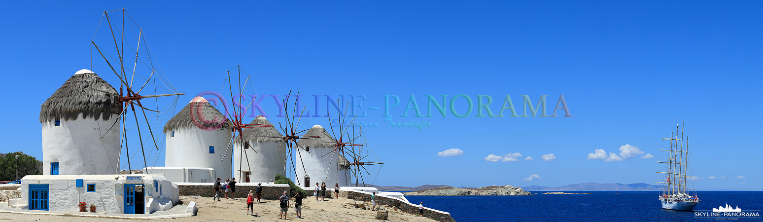 Die als Wahrzeichen bekannten fünf Windmühlen von Mykonos auf dem unteren Mühlenberg - auf diesem Panorama zu sehen mit einem Segelschiff, das vor der Bucht...