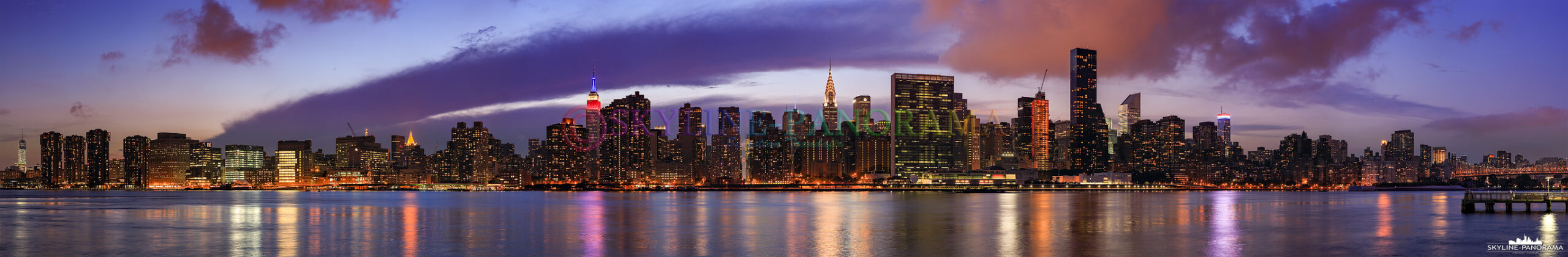 Panorama Manhattan - Die abendliche Skyline von Manhattan Midtown vom Gantry Plaza State Park in NY Queens gesehen. Von diesem Aussichtspunkt aus hat man einen fantastischen Blick auf die bekanntesten Wolkenkratzer von New York City – zum Beispiel das in den US - Nationalfarben Rot, Blau und Weiß beleuchtete Empire Sate Building, den Feedom Tower und das Chrysler Building - um nur einige zu nennen. 