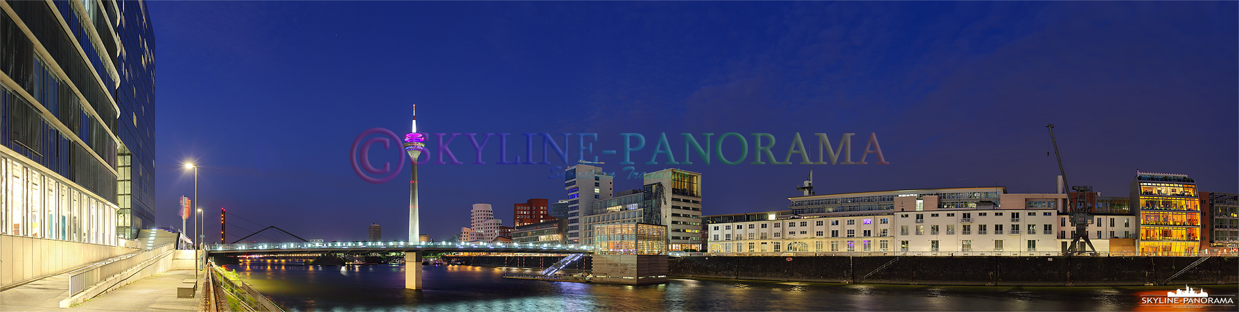 Panorama Düsseldorf - Eine abendliche Ansicht auf den beleuchteten Rheinturm und die Gehry-Bauten im Mediahafen von Düsseldorf.