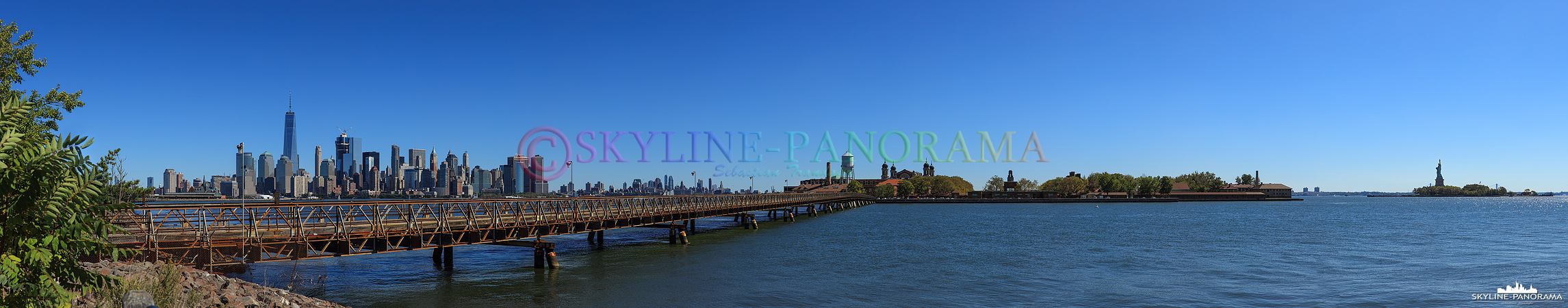 New York Skyline - Der Blick als Panorama von der Skyline Manhattans über Ellis Island zur Freiheitsstatue.