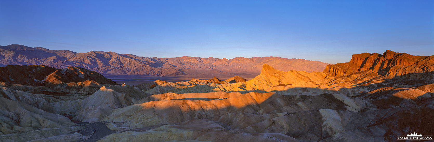Sehenswürdigkeiten im Death Valley - Einer der beliebtesten Aussichtspunkte im Death Valley Nationalpark in Kalifornien ist der Zabriskie Point, er bietet seinen Besuchern gerade zum Sonnenaufgang und Sonnenuntergang einen unvergesslichen Blick in das "Tal des Todes". Dieses 6x17 Panorama zeigt die von den ersten Sonnenstrahlen des Tages erleuchteten Berghänge der Panamint Range im Hintergrund und die durch Erosion entstandenen Gesteinsformationen der Amargosa Range im Vordergrund.