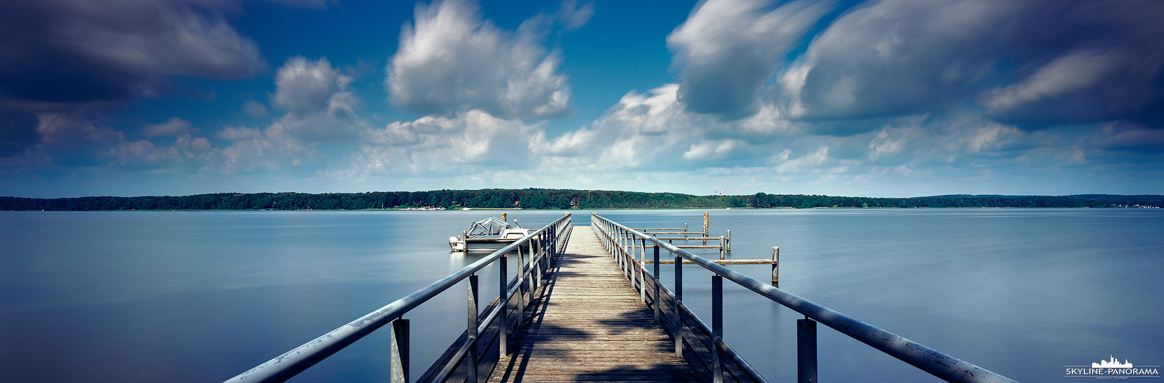 Der Scharmützelsee bei Bad Saarow in Brandenburg wird oft als märkisches Meer bezeichnet. Dieses Panorama eines Bootsstegs ist mit einer etwas längeren Belichtungszeit - in diesem Fall etwas über 2 Minuten - aufgenommen, wodurch sich die Wolken in Ihrer Bewegung abzeichnen und die Oberfläche des Sees glatt erscheint.