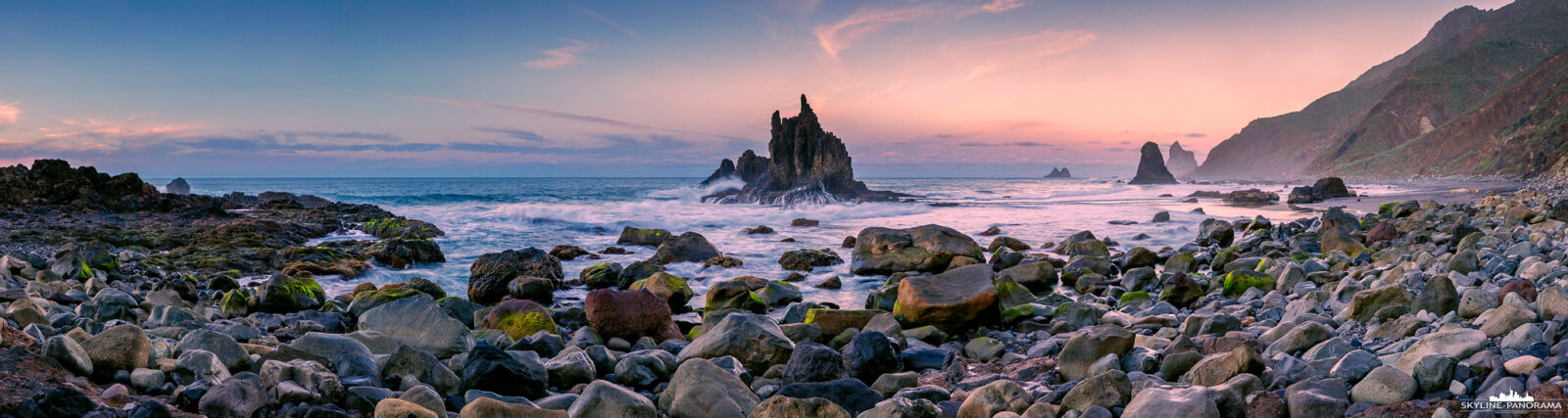 Playa de Benijo - Tenerife (p_01302) Tenerife Landscape - Dieses Panorama zeigt die raue Küstenlandschaft des Playa de Benijo während der abendlichen Dämmerung. Im Zentrum der Aufnahme ist die markante Felsformation Roque de Benijo zu sehen, sie zählt zu den bekanntesten Motiven im Nordosten von Teneriffa. Große Felsen des Steinstrandes prägen den Vordergrund und geben dem Panorama zusätzlich Tiefe und Struktur. Das weiche Licht der abendlichen Dämmerung erzeugt eine ruhige Atmosphäre und hebt die natürliche Form der Küstenlandschaft hervor.